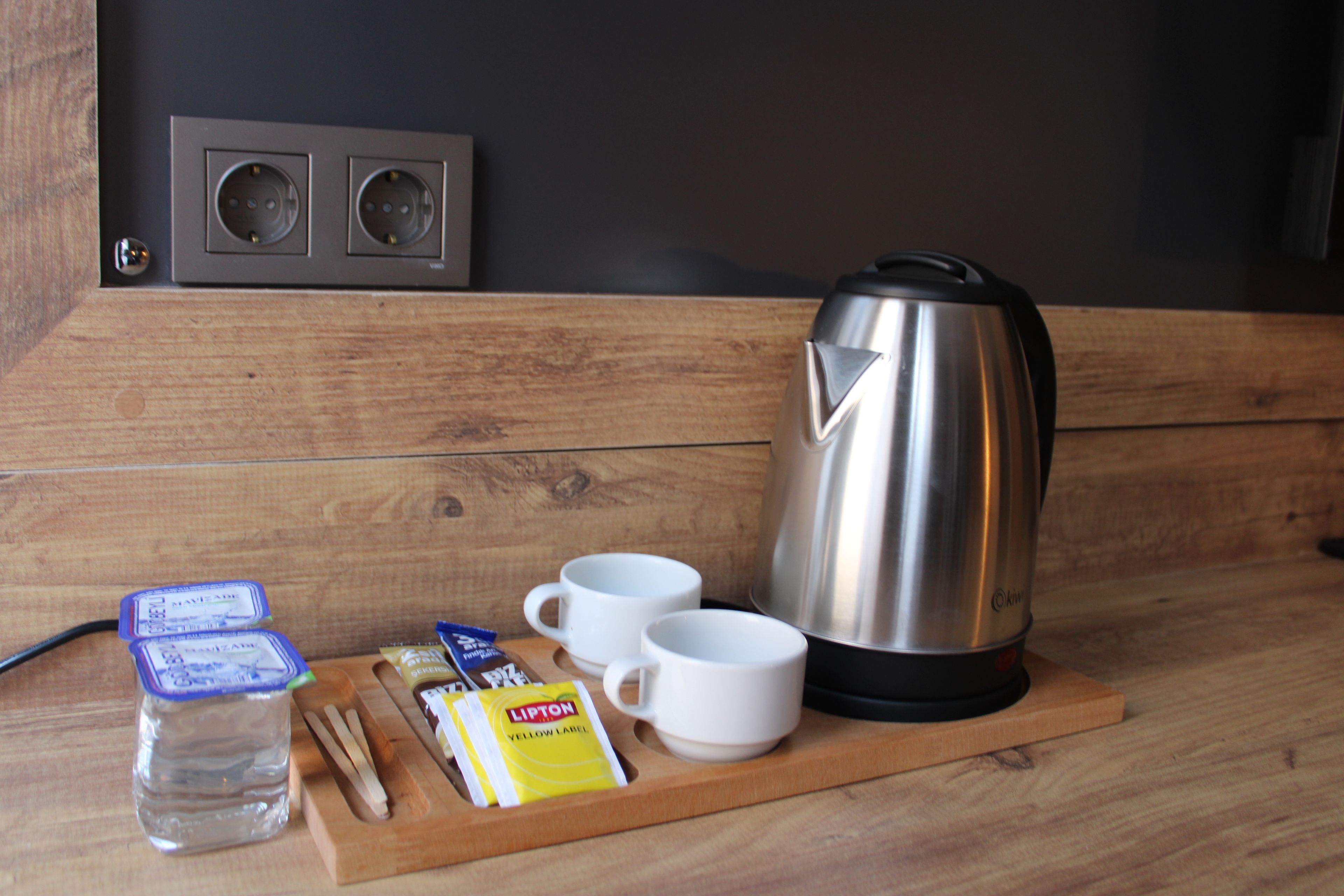 A wooden table with a kettle, two cups, a water bottle, and some snacks.