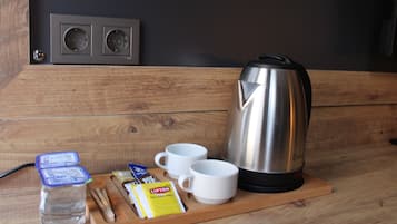 Una mesa de madera con una tetera, dos tazas, una botella de agua y algunos aperitivos.