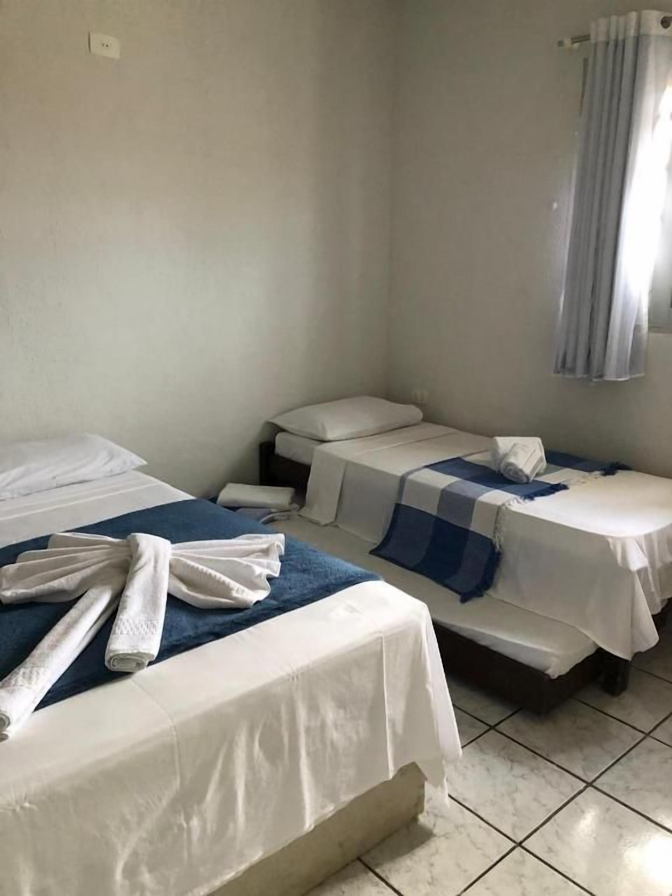 Habitación de hotel con dos camas, baño y ventana con cortinas.