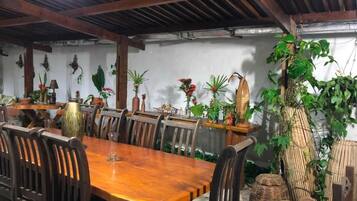 Un comedor con una mesa y sillas de madera, rodeado de plantas en macetas y objetos decorativos.
