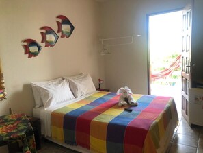 Quarto com cama, manta colorida, brinquedo de pelúcia, decoração de peixe na parede, guarda-roupa branco e porta que dá para uma varanda.