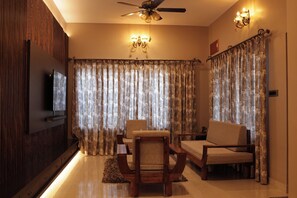 A living room with a television, two sofas, a dining table, and curtains. - Premium 2-Bedroom Apartment in Mysuru | Parking & WiFi (Mysuru)