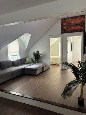 Ein modernes Schlafzimmer im Loft-Stil mit großem Fenster, Ecksofa, Topfpflanze und einem Gemälde.