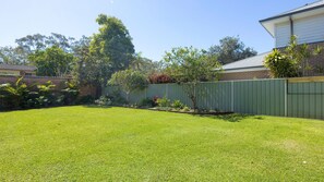A well-maintained backyard with a lawn, a green fence, and various plants. - Three Bays Retreat- Pet Friendly (Nelson Bay)