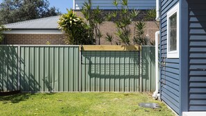 A fenced backyard with a grassy lawn, a brick wall, and a house with siding. - Three Bays Retreat- Pet Friendly (Nelson Bay)