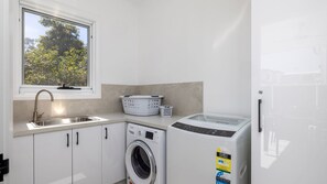 Una lavandería con lavadora, secadora, lavabo y cestas para ropa.