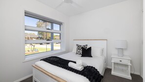 Un dormitorio con cama, mesita de noche, lámpara y ventana con persianas.