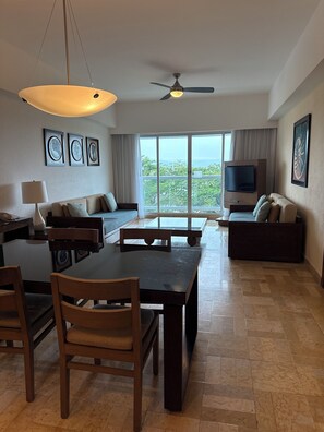 A modern living room with a dining area, a ceiling fan, large windows, and artwork on the walls. - Cozy 1-bedroom hotel suites with AC in cool Nuevo Vallarta, a lot of activities (Nuevo Vallarta)