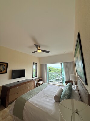 A hotel room with a bed, a television, a desk, a ceiling fan, a window with curtains, and a view of greenery. - Cozy 1-bedroom hotel suites with AC in cool Nuevo Vallarta, a lot of activities (Nuevo Vallarta)