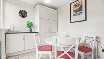 A modern kitchen with white cabinets, a round dining table, and red and white chairs.