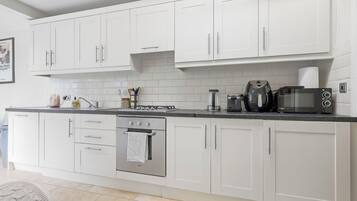 A modern kitchen with white cabinets, a gas stove, a built-in oven, a coffee maker, and a microwave.