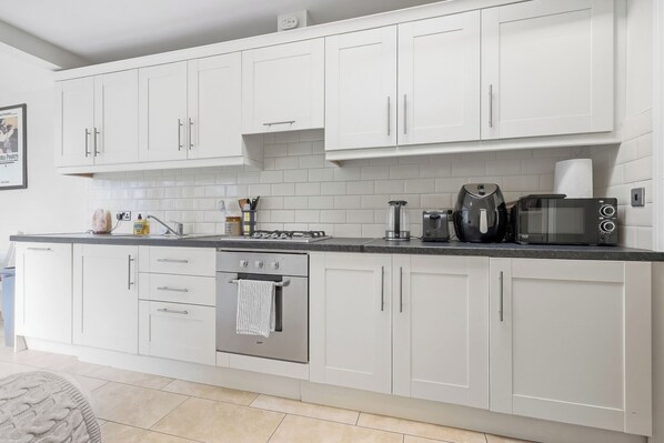 A modern kitchen with white cabinets, a gas stove, a built-in oven, a coffee maker, and a microwave.