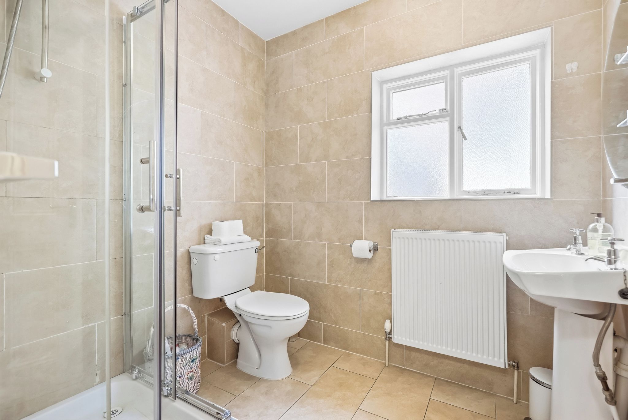 A bathroom with a shower, toilet, radiator, and a window.