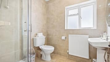 A bathroom with a shower, toilet, radiator, and a window.