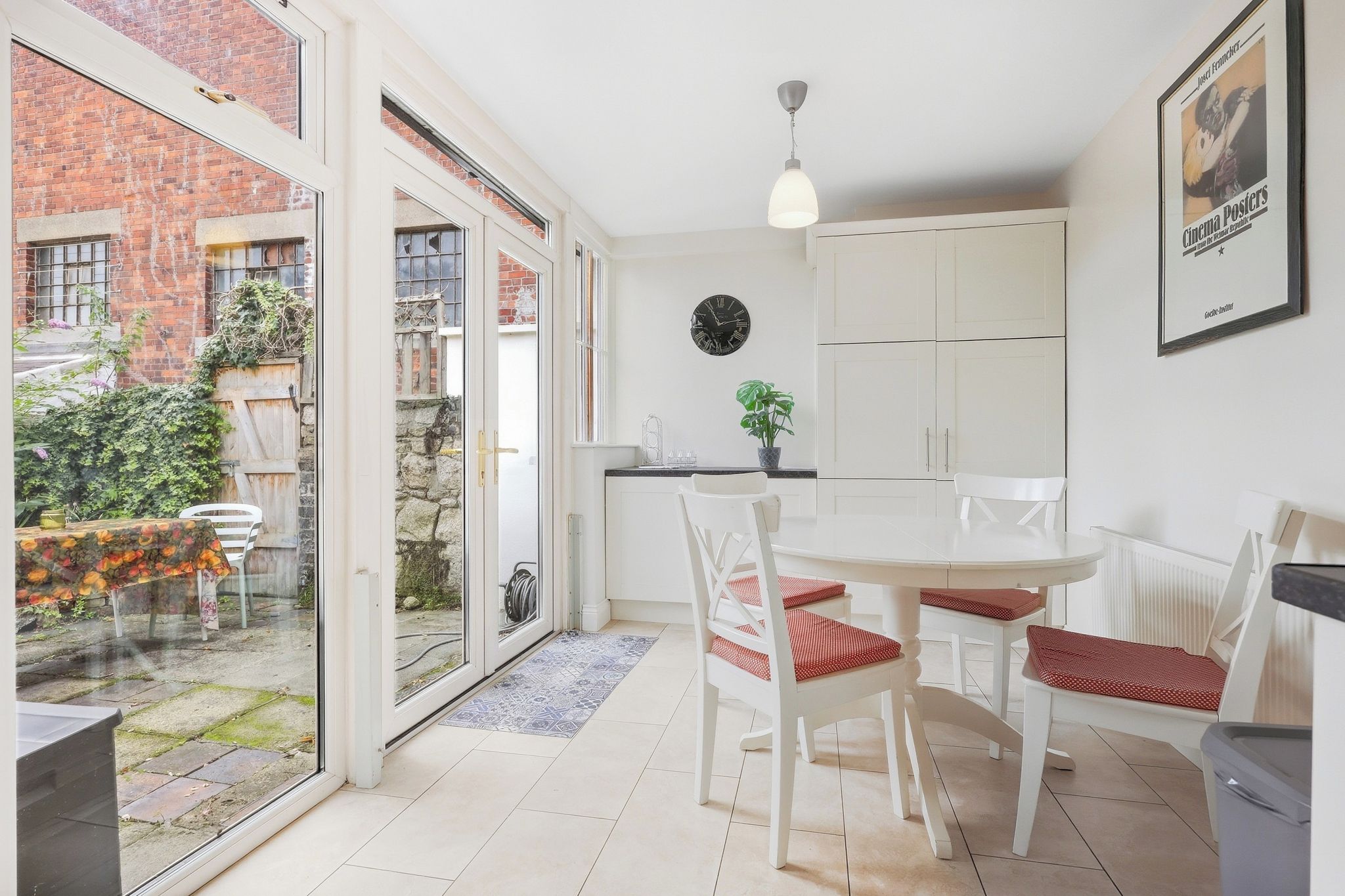 A modern kitchen with white cabinets, a dining table with chairs, and a large window overlooking a garden.