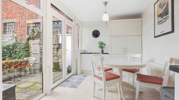 A modern kitchen with white cabinets, a dining table with chairs, and a large window overlooking a garden.