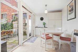 A modern kitchen with white cabinets, a dining table with chairs, and a large window overlooking a garden.