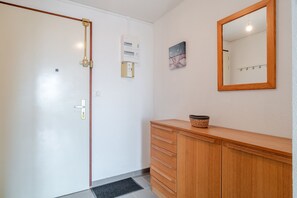 A room with a wooden cabinet, a mirror, a door with a handle, and a wall-mounted electrical box. - L'Horizon de Pentrez -charmant duplex proche plage (Saint-Nic)