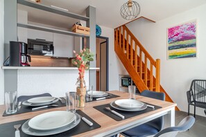 A modern dining area with a wooden table set for two, a coffee machine, and a view of a staircase. - L'Horizon de Pentrez -charmant duplex proche plage (Saint-Nic)