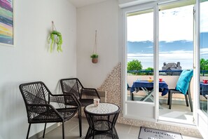 A room with a view of the sea, featuring a table and chairs, a hanging plant, and a welcome mat. - L'Horizon de Pentrez -charmant duplex proche plage (Saint-Nic)
