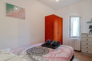 A bedroom with a bed, a wardrobe, a radiator, and a window with curtains. - Patio Iodé - Appart bord de mer avec terrasse (Saint-Nic)