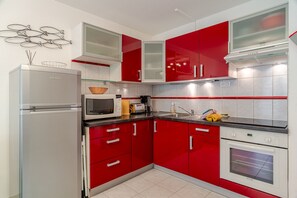 A modern kitchen with red cabinets, a white refrigerator, and a built-in oven. - Patio Iodé - Appart bord de mer avec terrasse (Saint-Nic)