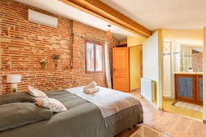 Ein Schlafzimmer mit Ziegelwand, einem Bett mit Kissen, einem Fenster und einer Holztür.