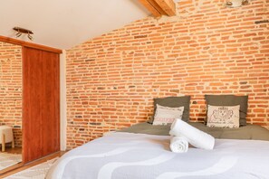 Ein Schlafzimmer mit Backsteinwand, einer Holztür, einem Bett mit weißer Decke und zwei Kissen mit dekorativen Mustern.