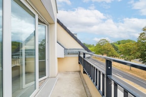 A balcony with a glass door, a metal railing, and a view of a road and trees. - L'Escale Beauvaisienne - parking privé (Beauvais)