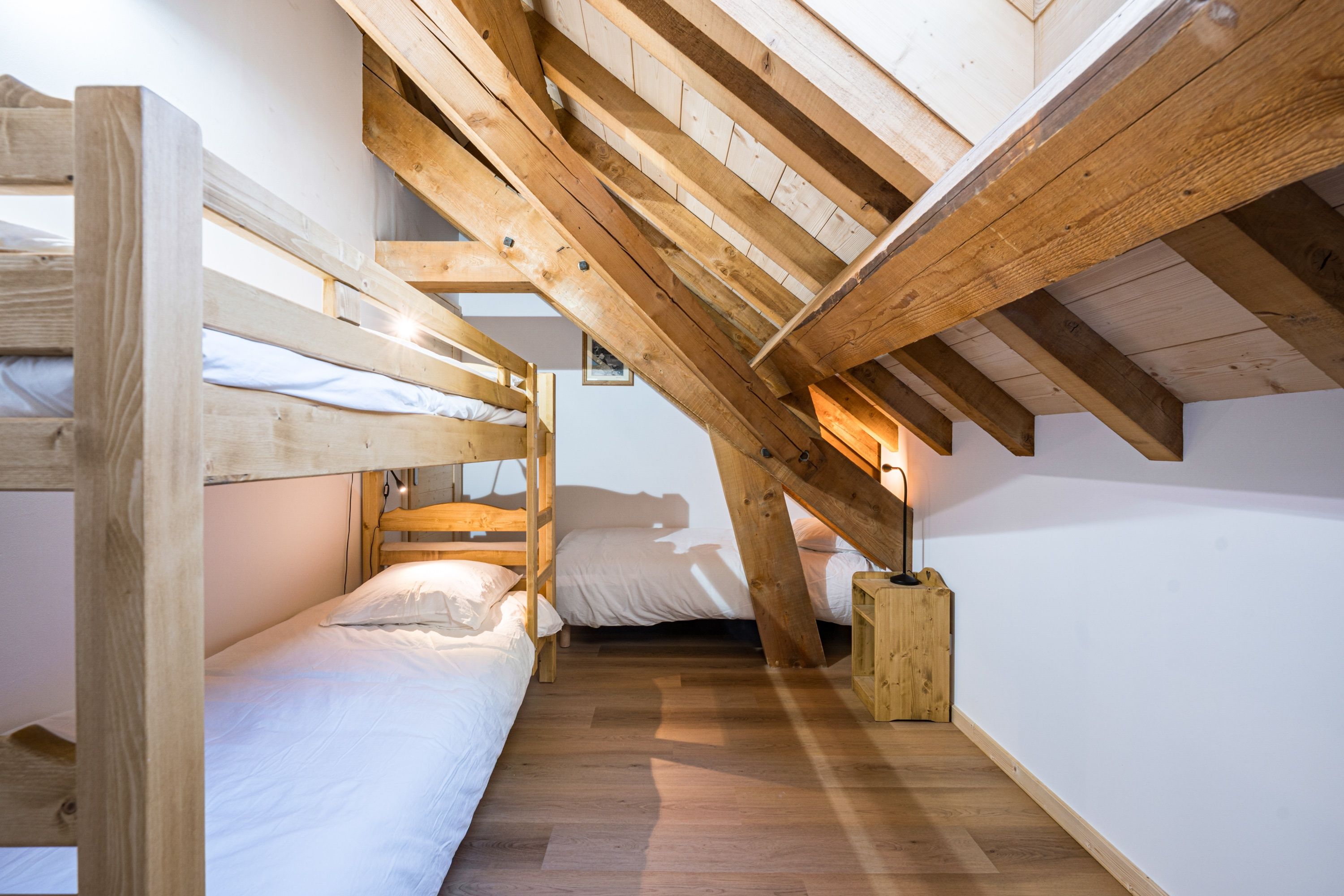 Une chambre de dortoir avec des lits superposés, des poutres en bois et une petite table de chevet.