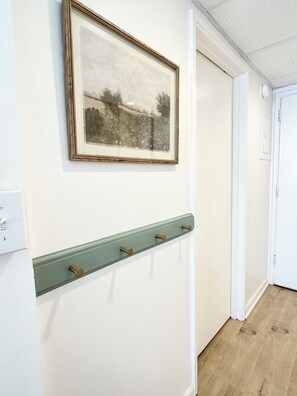 Een gang met een afbeelding in een lijst aan de muur, een lichtschakelaar en een deur aan het einde.