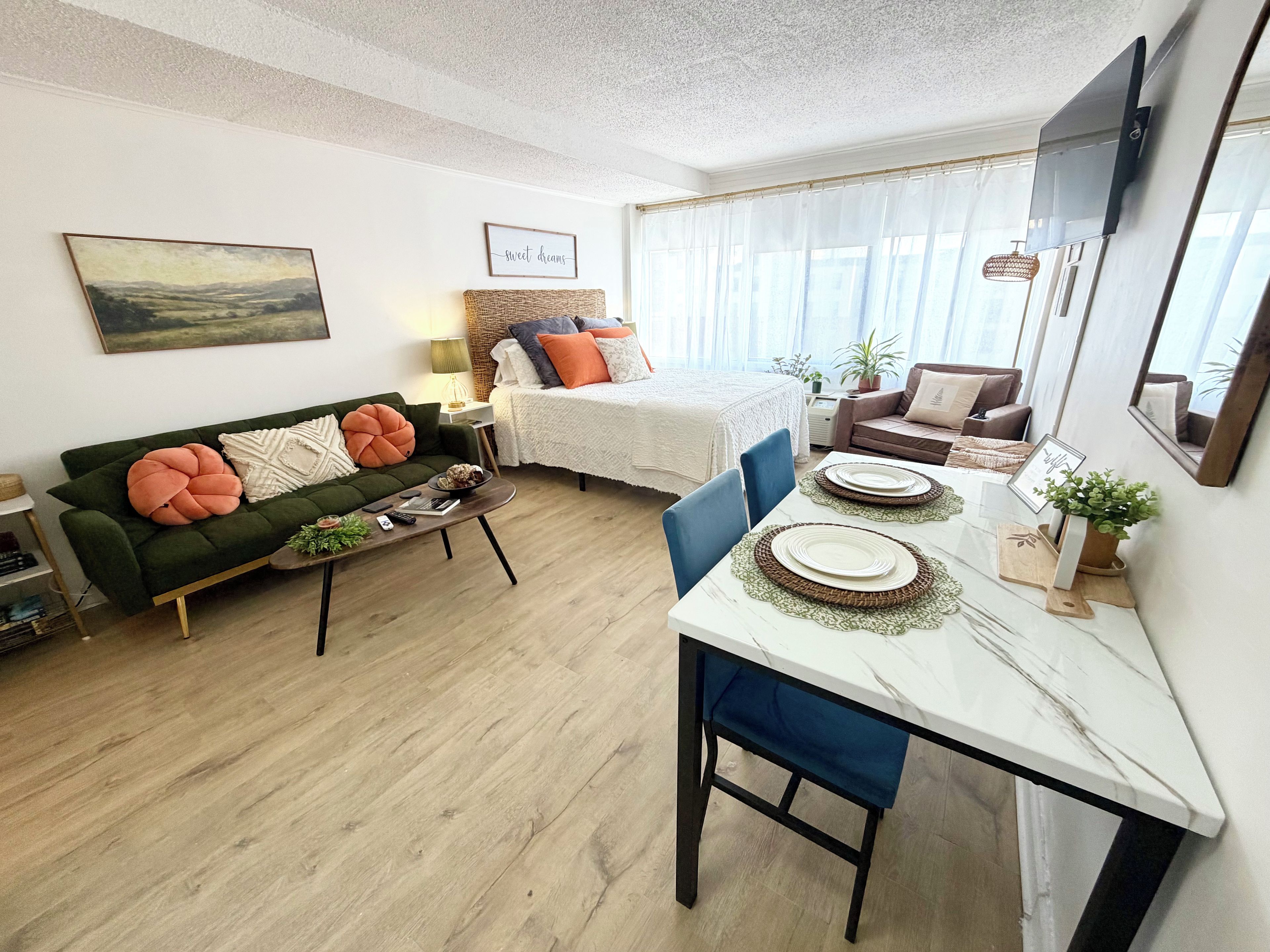 Una sala de estar moderna con un sofá, una mesa de comedor con platos, una cama con edredón blanco y un cuadro en la pared.