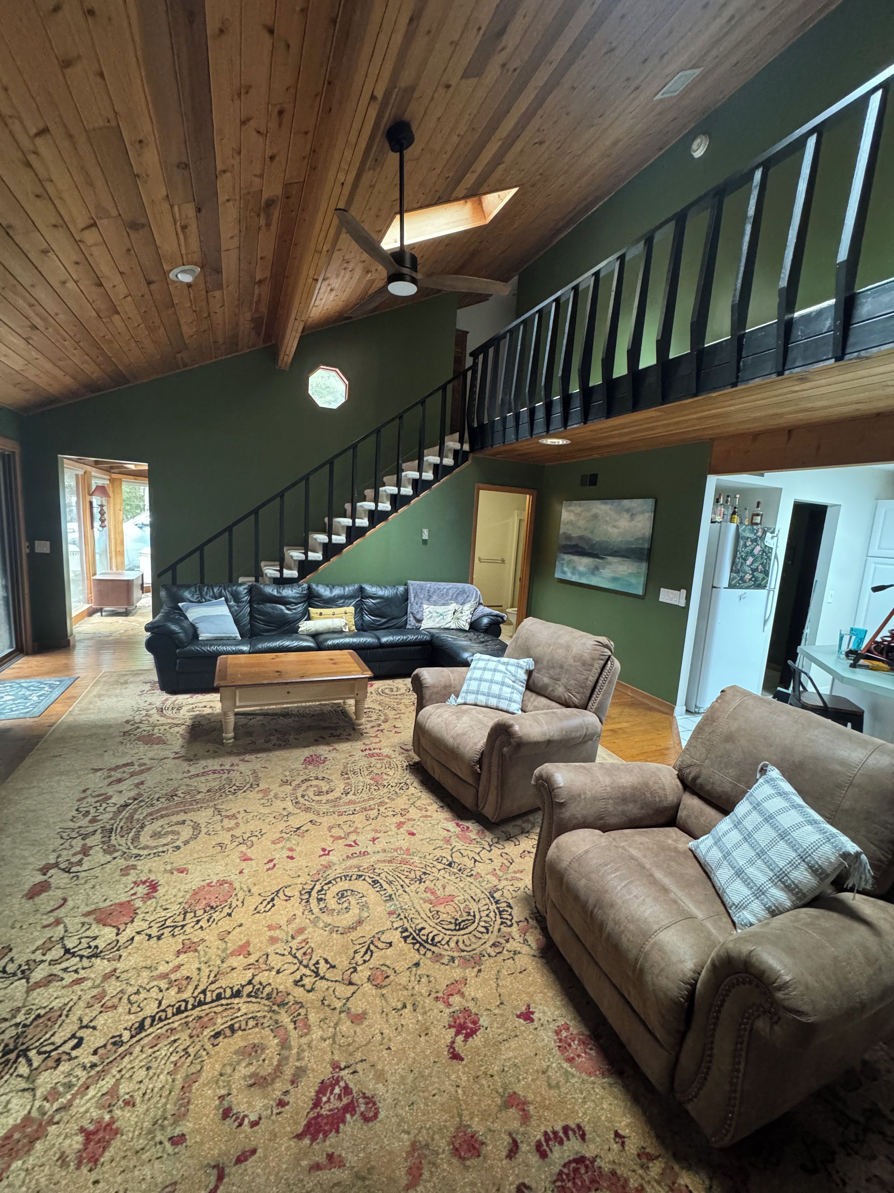 A spacious living room with a high ceiling, a wooden staircase, and a large rug.