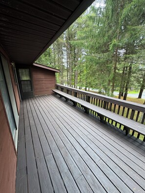 Eine Holzterrasse mit Geländer, einer Bank und Blick auf einen Wald.