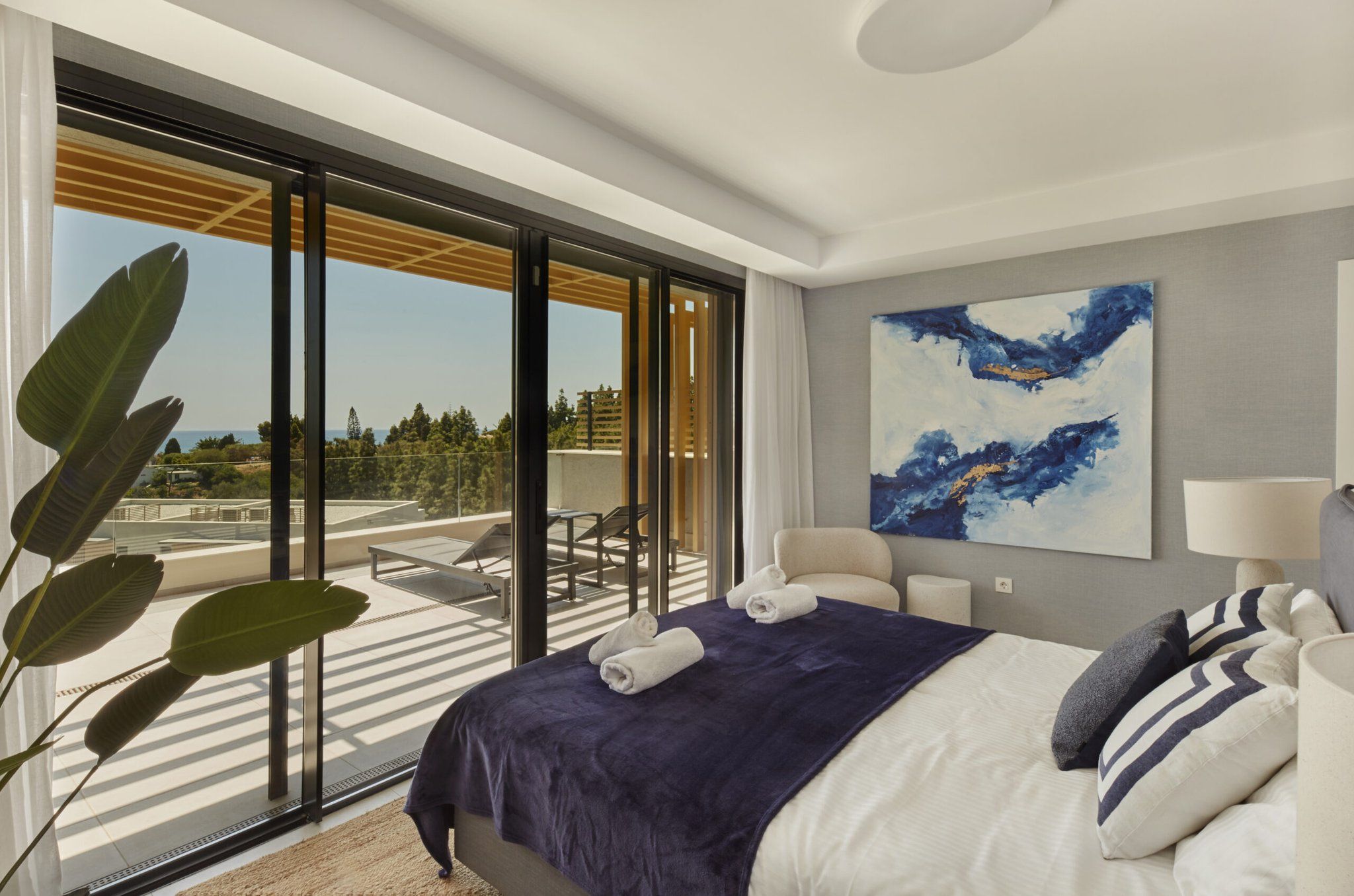 A modern hotel room with a large bed, a view of the outdoors, and a painting on the wall.
