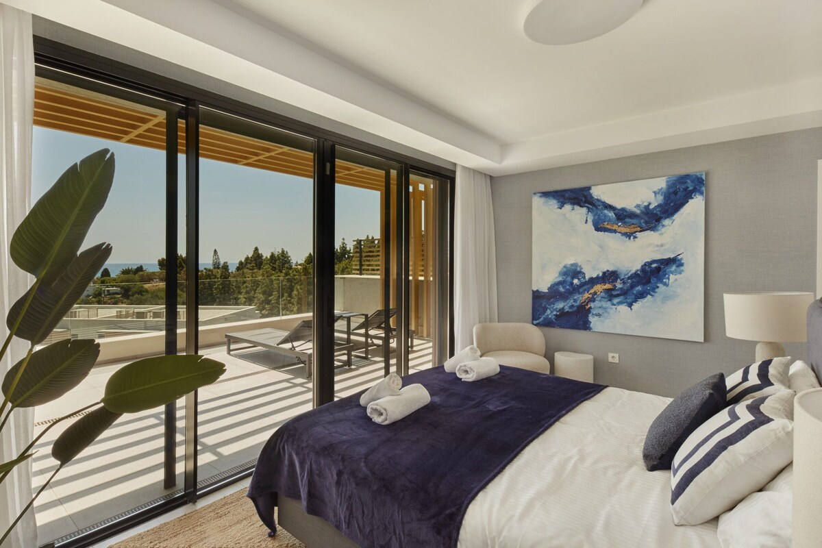 A modern hotel room with a large bed, a view of the outdoors, and a painting on the wall.