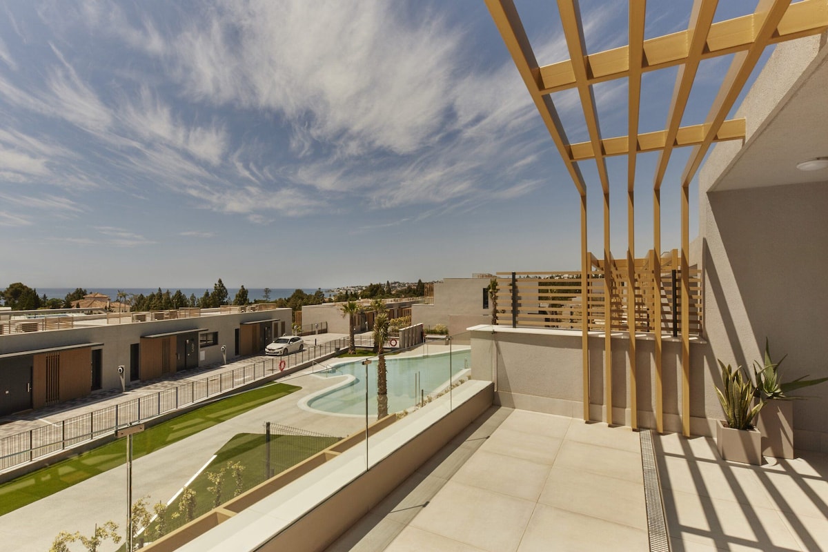 A rooftop terrace with a pool, a view of the sea, and a modern building structure.
