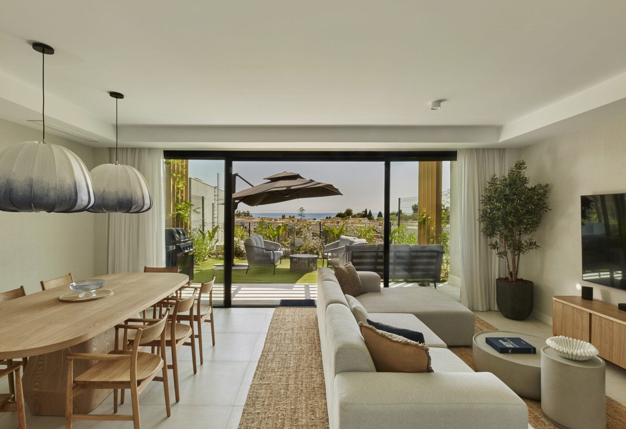 A modern living room with a dining area, large sliding glass doors leading to an outdoor space, and a flat-screen TV on a wooden console.