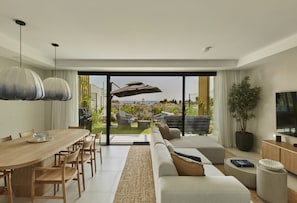 A modern living room with a dining area, large sliding glass doors leading to an outdoor space, and a flat-screen TV on a wooden console. - IIM Residences El Chaparral (Mijas)