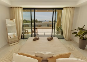 A bedroom with a large bed, a sitting area, a balcony with a view, and a potted plant. - IIM Residences El Chaparral (Mijas)