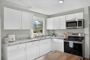 A modern kitchen with white cabinets, a granite countertop, a built-in microwave, a stove, and a window with a view of greenery. - Spacious 3BR Home with Full Kitchen and Carport (Abilene)