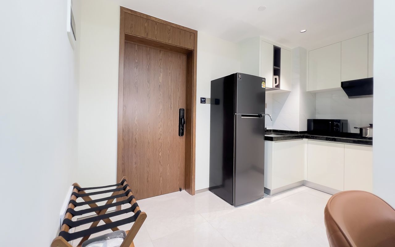 A modern kitchen with a black refrigerator, wooden door, and white cabinets.