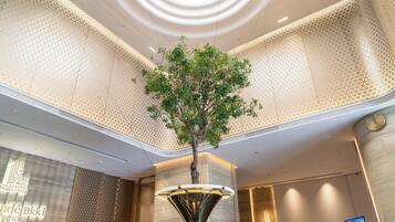 A lobby with a decorative tree, a reception desk, and a modern chandelier.