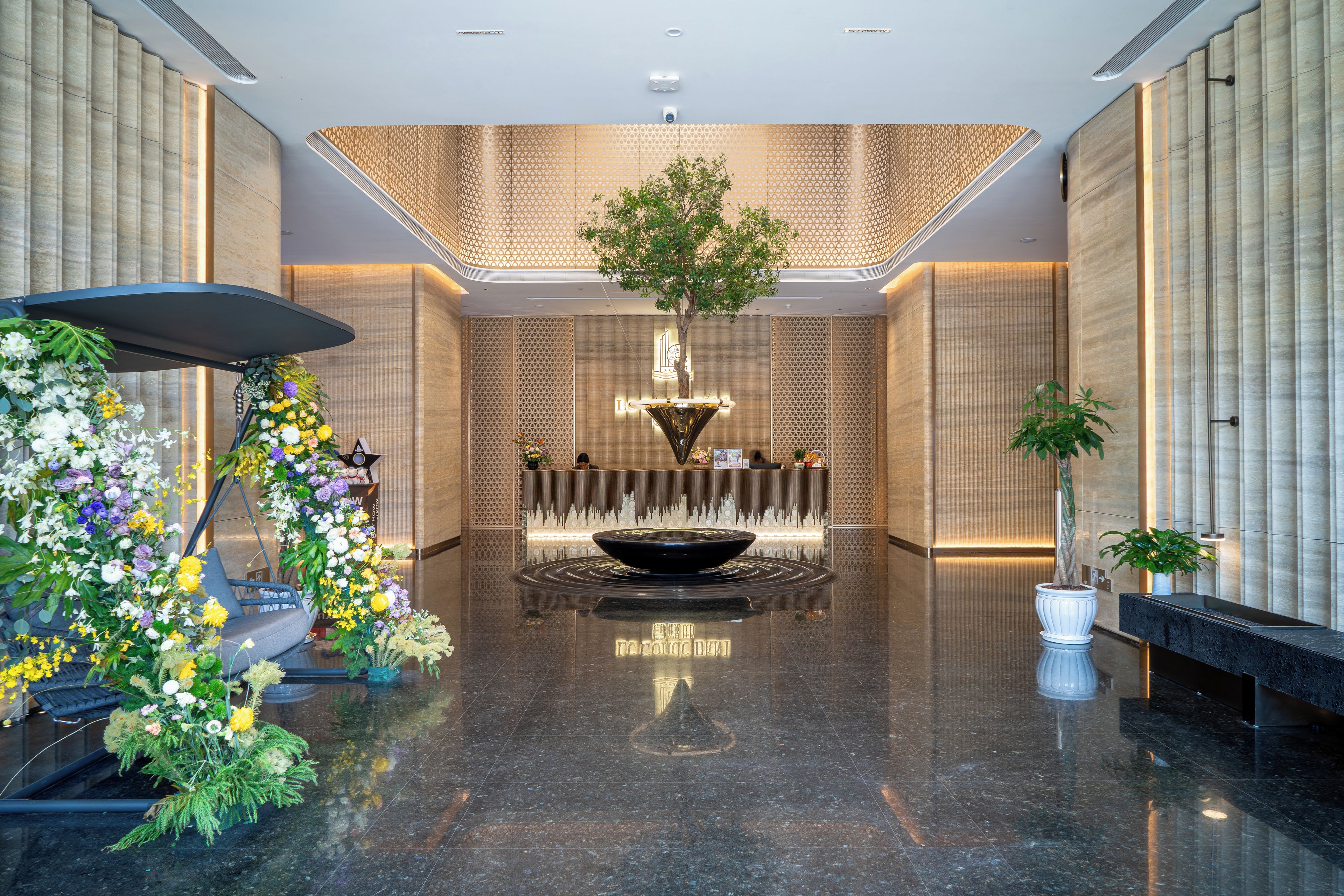Un vestíbulo moderno con una recepción, una fuente decorativa y diversas plantas.