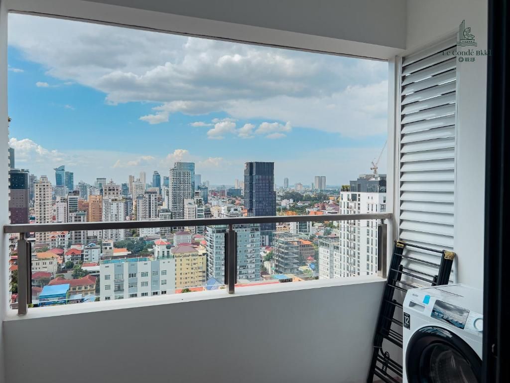 Un balcon avec vue sur la ville, un lave-linge et une fenêtre avec des stores.