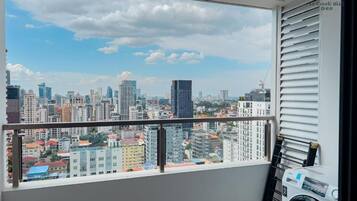 Un balcon avec vue sur la ville, un lave-linge et une fenêtre avec des stores.