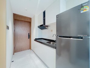 A kitchen with a stainless steel refrigerator, a wooden door, and a black range hood. - Le Condé Maison (Phnom Penh)