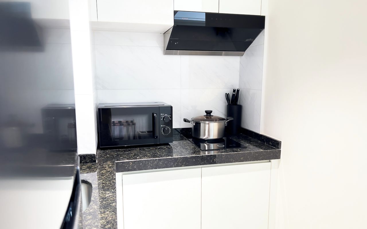 Una cocina con microondas, una olla en la estufa y una campana extractora negra.