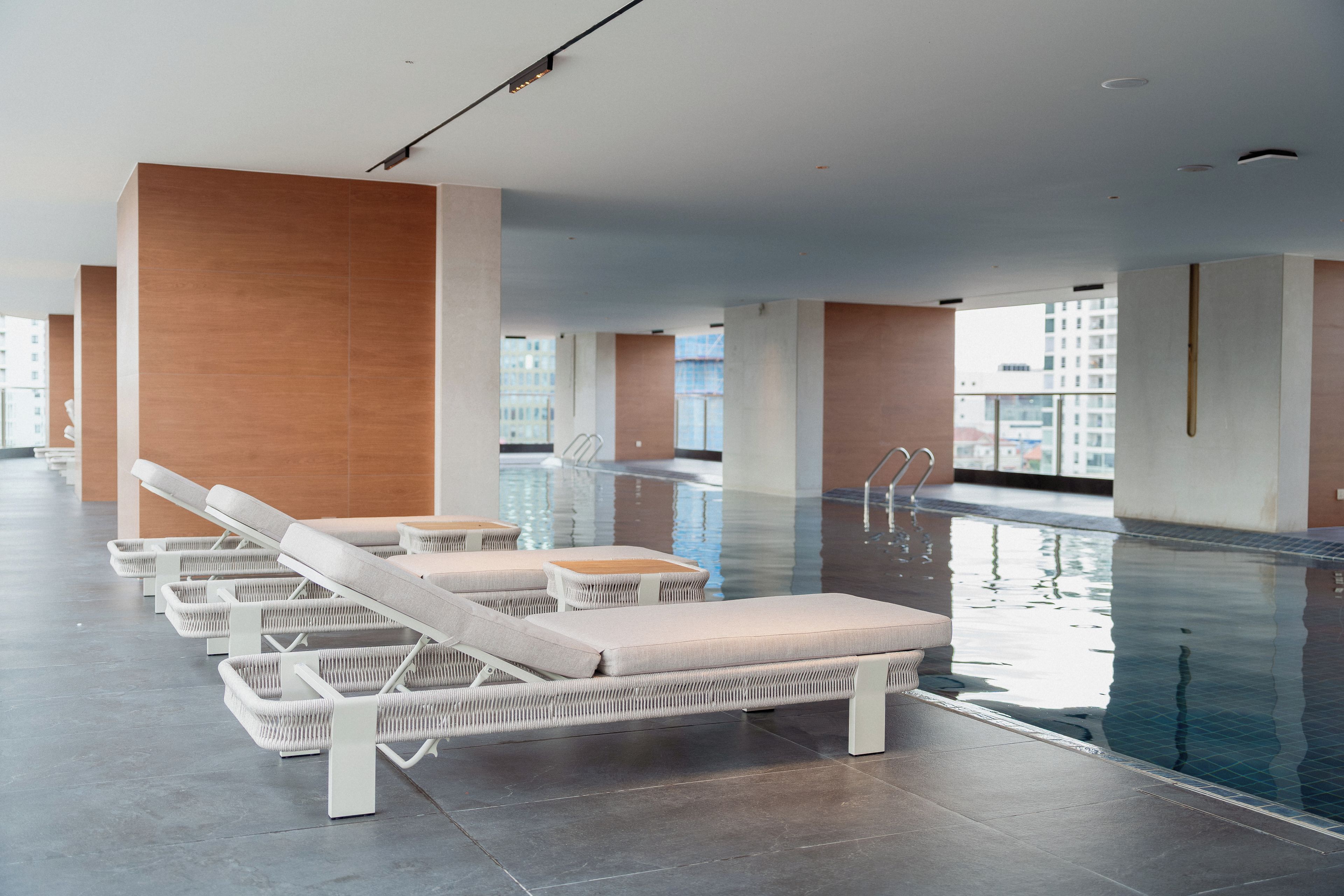 Una piscina interior moderna con sillones de descanso y vista despejada del paisaje urbano.
