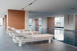 Una piscina interior moderna con sillones de descanso y vista despejada del paisaje urbano.
